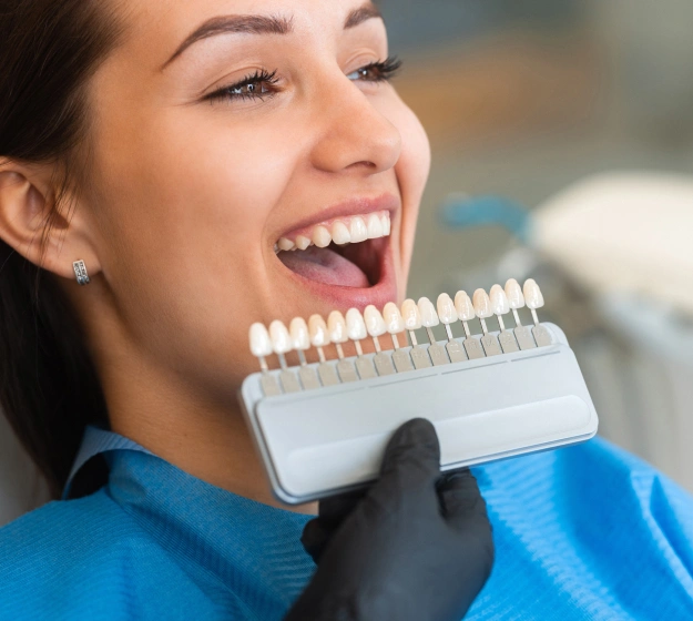 Woman smiling while holding dental shade guide for tooth color matching at dentistry office.