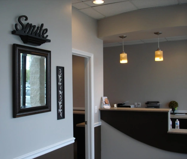 Modern dental office reception area with curved black desk, pendant lighting, and welcoming smile signage.