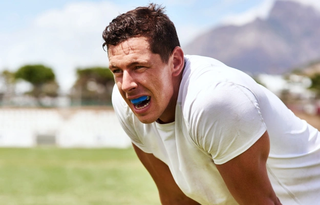 Man in white shirt displaying bright smile outdoors on grass field.