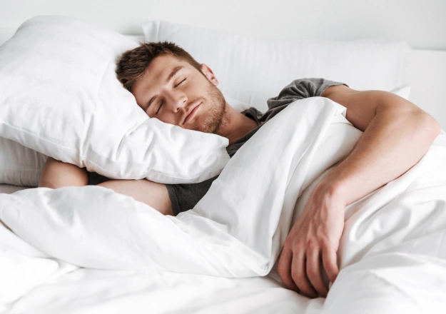 Man sleeping peacefully in bed with white pillows and bedding.