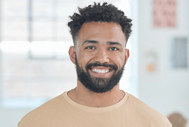 Smiling man in beige shirt against blurred office background at dental practice.