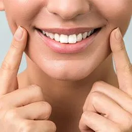 Person smiling brightly while pointing to teeth, displaying healthy dental results in close-up portrait.