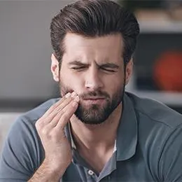 Man with beard touching his cheek in discomfort, suggesting dental pain or toothache.
