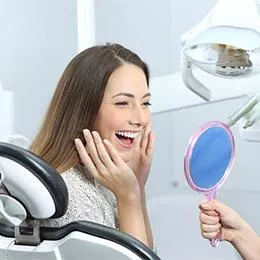 Woman smiling at dental mirror in modern dentist office examining her teeth.