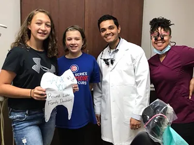Four people in dental office holding white item, smiling at camera indoors.