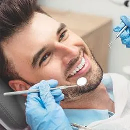Male patient receiving dental examination from dentist wearing blue gloves in clinical setting.