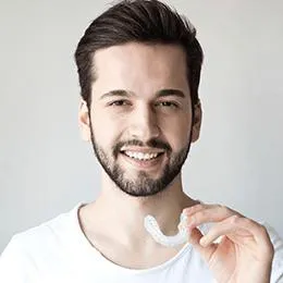 Man smiling while holding dental floss against neutral background for dentistry website.