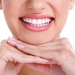 Young person displaying a bright, healthy smile with hands framing their face against pink background.